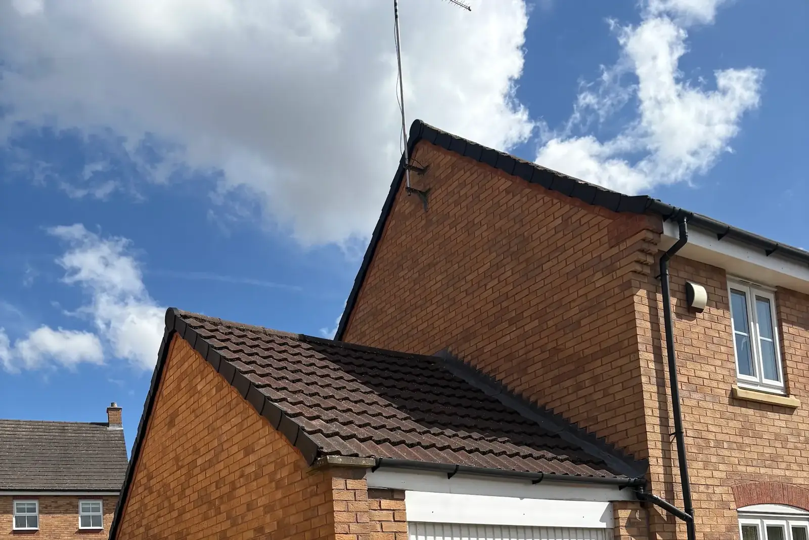 A newly tiled garage roof beside a brick house, finished by Property Fix Roofing Solutions Ltd